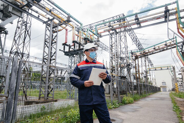 An electrical substation engineer inspects modern high-voltage equipment in a mask at the time of...