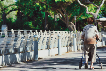 elderly woman walking and using a walker in a park, disability
