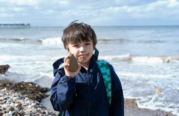Kid with dirty mount of chocolate ice cream showing stone to the beach on spring or summer, Child boy playing with the rock, Children exploring by the seaside, Play and lean from nature