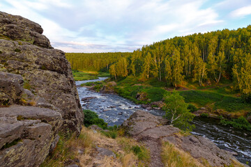 Fototapeta na wymiar soft sun rays in evening over beautiful valley with mountain river and many rapids. Ural, Russia,
