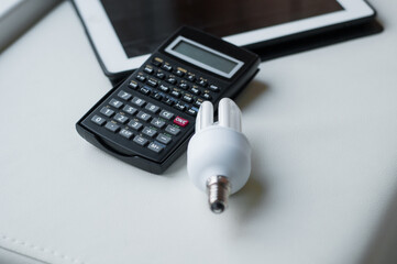 Energy efficiency rating chart, LED light bulb and calculator on white background, closeup