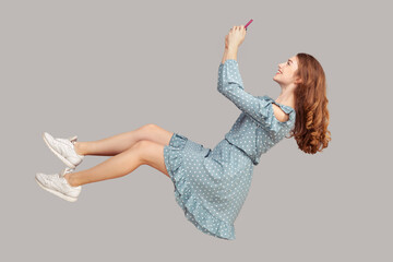 Hovering in air. Smiling girl ruffle dress levitating with mobile phone, reading message chatting...