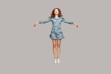 Full length happy calm pretty girl in vintage ruffle dress levitating hovering in mid-air with raised hands as wings, jumping trampoline or flying up. indoor studio shot isolated on gray background - obrazy, fototapety, plakaty