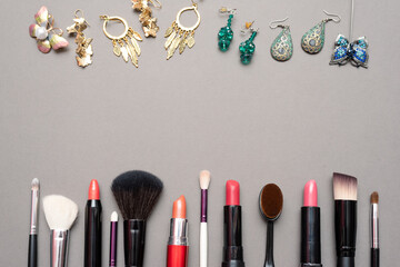 Makeup brushes, lipstick and bijouterie on the gray flat lay background with copy space.