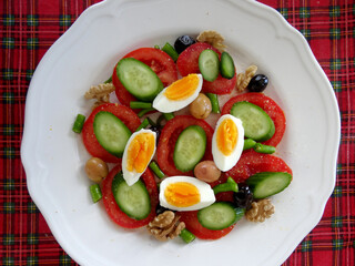 A healthy Mediterranean diet plate with tomatoes, cucumbers, peppers, balck and green olives. walnuts and eggs.