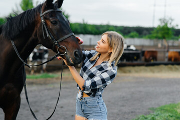 Obraz premium A young pretty girl rider poses near a thoroughbred stallion on a ranch. Horse riding, horse racing