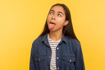 Portrait of funny dumb crazy girl in denim shirt showing tongue out and looking cross-eyed with...