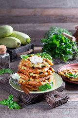 Zucchini waffle, zucchini fritters cooking on waffle maker with sour cream with basil on a plate