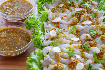 Top view of raw shrimp on top with spicy fish sauce, garlic and fresh coriander, and Thai style seafood sauce on side. 