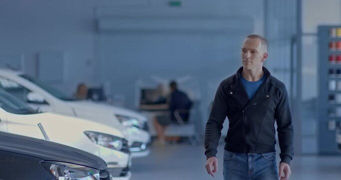Young man goes to a car dealership and watches a car, chooses a new auto. Male businessman walks around a car dealership, wants to make a purchase. Car business.