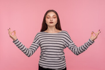 Inner peace, yoga meditation. Portrait of tranquil woman in striped sweatshirt holding hands in mudra gesture and practicing mental health, breath techniques. studio shot isolated on pink background