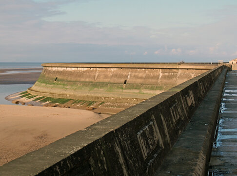 the seawall in blackpool with the beach at low tide in sunlight with the wall of the old boat pool