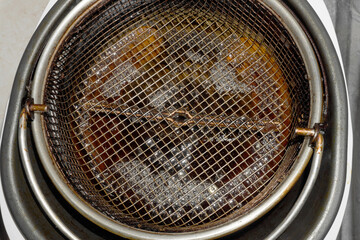 Dirty coating grate in deep fryer. Dark brown oil. Fast food. Obesity problems. Health hazards, fatty foods. Untimely replacement, bad faith. Blur at the edges.