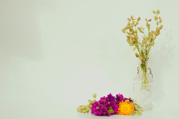 Photo with flowers: calendula blossom and mallow branch at the front, grass with small bulbs in a vintage glass bottle.