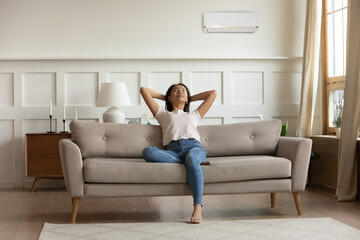 Happy young calm woman relaxing on sofa, breathing fresh air, satisfied with comfortable indoors...