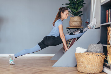 Flexible woman doing front split stretching exercise at home.
