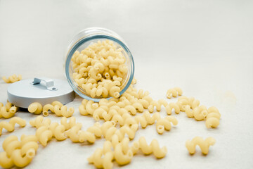 Unprepared traditional Italian pasta cellentani scattered on a light background near a glass jar with a metal lid.