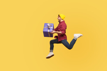 Enthusiastic extremely joyful hipster guy running quickly fast with gift box, flying in air holding birthday present surprise, hurry to give holiday bonus. full length studio shot isolated on yellow