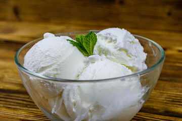 Glass bowl with ice cream balls and mint leaf on a wooden table