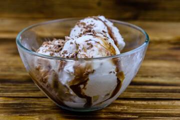 Glass bowl with ice cream balls and chocolate topping on a wooden table