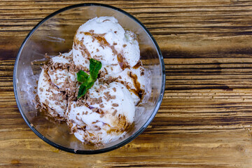 Glass bowl with ice cream balls, mint leaf and chocolate topping on a wooden table. Top view