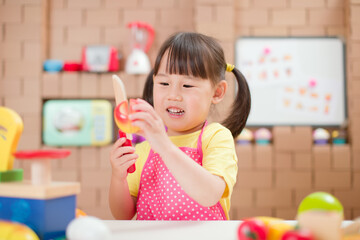 toddler girl pretend play food preparing role against cardboard blocks kitchen background