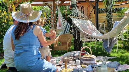 Rodzinny piknik w ogrodzie wśród zieleni i śpiewu ptaów, latem w cieniu drzew, odpoczynek na hamaku, koszyk piknikowy