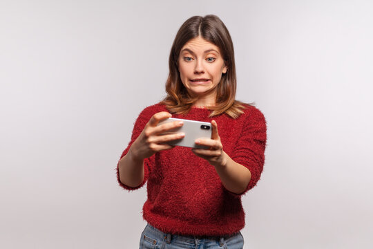 Oops, sorry! Frustrated woman in shaggy sweater looking at smartphone with excuse grimace, feeling helpless with device, mobile program application. indoor studio shot isolated on gray background