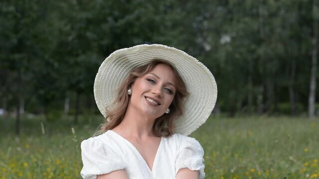 Beautiful girl portrait in a big white hat looks at the camera in a summer park on the lawn, beautiful smile and laugh
