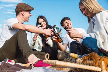 Happy multiracial friends having fun on a picnic - Youth toasting with beer and using their smart phones - Friendship concept in the fresh entertainment mood - Focus on the youth ahead