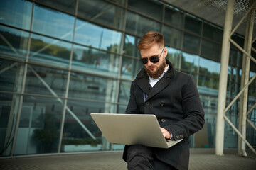 Manager holding laptop, Out of office work, young businessman in sunglasses using computer for his job at outside. Handsome bearded hipster, Communication and technology, in the open air, Surfing