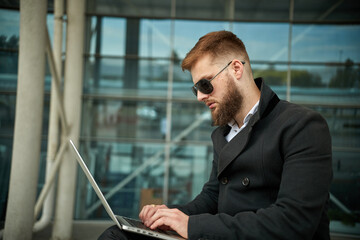 Manager holding laptop, Out of office work, young businessman in sunglasses using computer for his job at outside. Handsome bearded hipster, Communication and technology, in the open air, Surfing