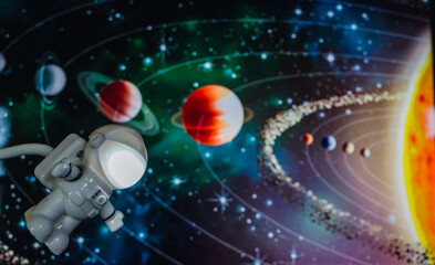 Little toy astronaut traveling through space, with a background of the planets of the solar system