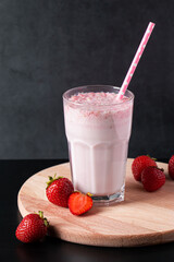 Fresh milkshake with strawberries on black background. Summer drink with a straw in a glass. Place for text.