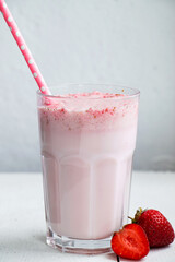 Cold milkshake with strawberries on white background. Summer drink in a glass with a paper straw.
