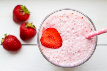 Cold milkshake with strawberries on white background. Summer drink in a glass with a paper straw.