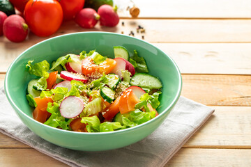 Recipe for vegetable salad with tomatoes, cucumbers and radishes. Seasonal dish on wooden background. Vegan food for diet.