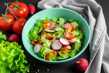 Fresh vegetable salad in a ceramic bowl on gray background. Seasonal summer dish of tomatoes, cucumbers and radishes.