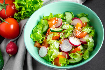 Seasonal vegetable salad from organic farm products on gray background. Mix of tomatoes, cucumbers and radishes.