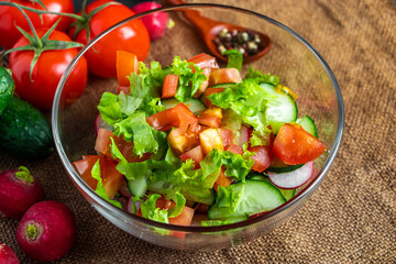 Seasonal summer vegetable salad in a glass bowl on dark background. Vegan organic food, dietary meal in a rustic style.
