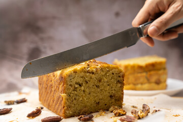 Hand with knife ready to slice a piece of banana walnut pound cake