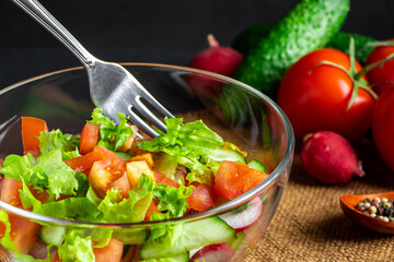 Seasonal summer vegetable salad in a glass bowl on dark background. Vegan organic food, dietary meal in a rustic style.