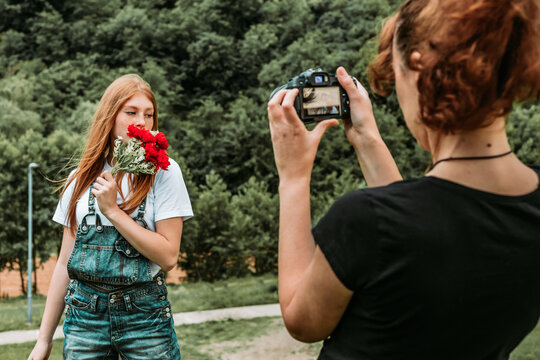 Female photographer taking photos of teen ginger girl holding bouquet of roses.