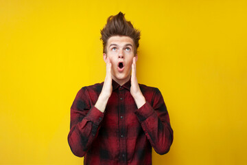 crazy guy with a funny hairstyle is surprised on a yellow isolated background, hipster with strong hair styling is shocked