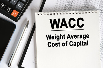 On the table lies a smartphone, a calculator and a notebook with the inscription- WACC.