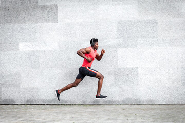 African American guy runner runs fast forward against the background of the city wall, sports man...
