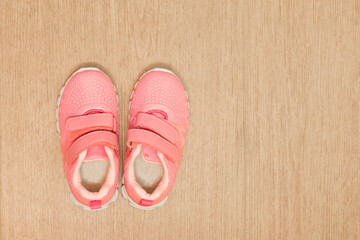 New pink kids sneakers on a light brown floor. View from above. Copy space on the right.