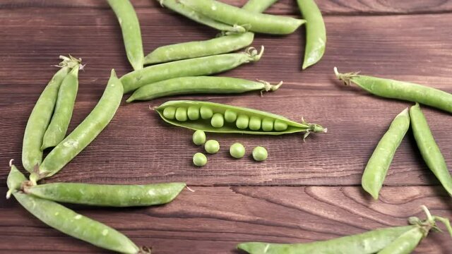 An open pea pod with grains next to other pods on a brown wooden background. Close-up