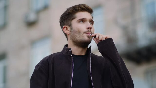 Handsome man vaping outdoors. Thoughtful guy smoking e-cigarette on city street