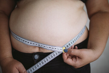 Overweight woman measuring waist with measure tape, close up image. Weight loss, motivation, fat burning
